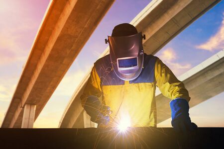 Industrial Worker with safety equipments and protective mask welding steel structure with expressway...