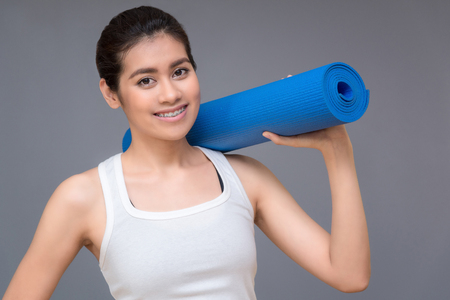 Young asian woman with happy smile holding her yoga mat at yoga healthy sport gym. Yoga and meditation have good benefits for health. Photo concept for Yoga Sport and Healthy lifestyle.の写真素材
