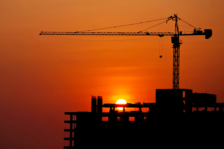 Silhouetted construction crane and building at construction site on sunset for construction industrial work conceptの写真素材