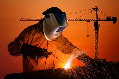 Welding worker welding steel structure with construction crane and building at construction site on...