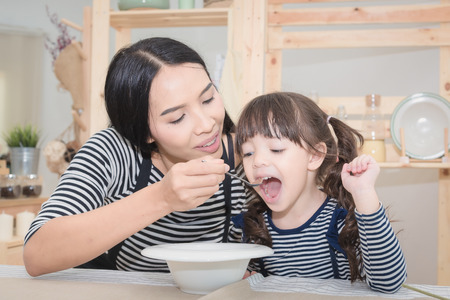 Happy family of asian mom feeding healthy breakfast to her cute daughter in the morning. Photo series of family, kids and happy people concept.の写真素材