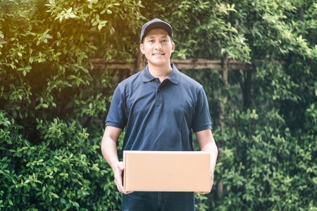 Handsome young asian delivery man smiling while holding a cardboard box delivery to his customer.の写真素材
