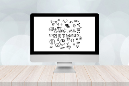 Smart modern pc with social network doodle on screen on wooden table and modern bokeh wall in background.の写真素材