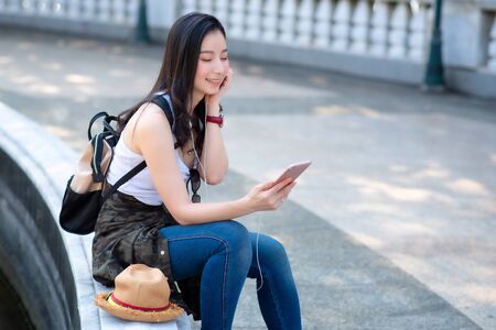 Beautiful asian tourist woman relaxing and enjoying listening the music on a smartphone in urban city downtown. Vacation travel in summer.の写真素材