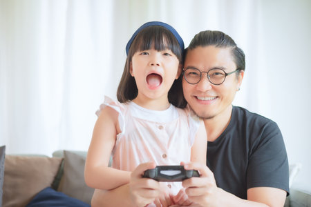 Asian Father and cute daughter enjoy and play console game on vacation at homeの写真素材