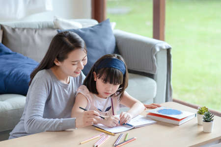Asian mother teaching her cute kid daughter to studying in living room at homeの写真素材