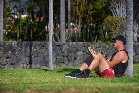 Sportsman sitting on the grass reading a book in the park