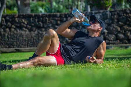 Athlete man lying on grass drinking water in parkの写真素材