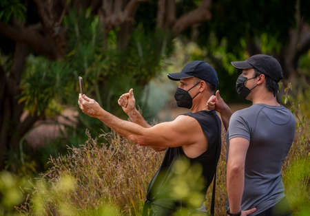 Men in masks in the park doing sport and taking a selfie with a smartphoneの写真素材