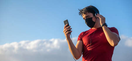 Boy with mask, headphones and smartphone listening to music in the nature with blue skies