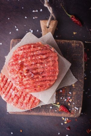 Raw Ground beef meat Burger steak cutlets with seasoning on vintage wooden boards, black の写真素材