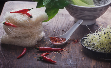 Oriental style lunch preparattion: rice noodles, chili pepper, moyashi, bok choi, moyashi springs and shimeji mushrooms on the rustic wooden boardの写真素材