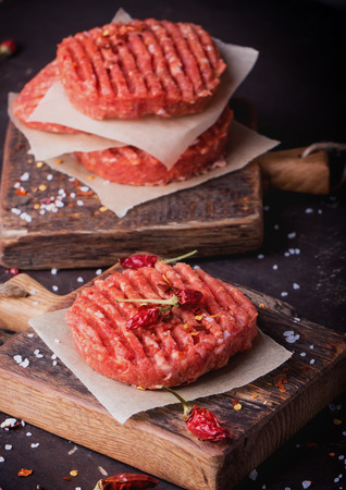Raw Ground beef meat Burger steak cutlets with seasoning on vintage wooden boards, black backgroundの写真素材