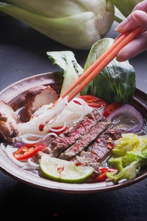 Vietnamese Pho Bo soup served in vintage oriental bowl with chop sticks, seasoning and greens on backgroundの写真素材
