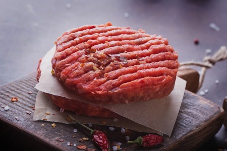 Raw Ground beef meat Burger steak cutlets with seasoning on vintage wooden boards, black backgroundの写真素材