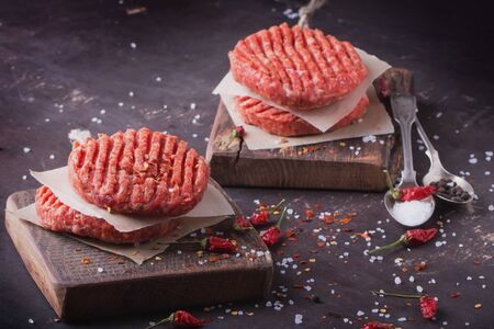 Raw Ground beef meat Burger steak cutlets with seasoning on vintage wooden boards, black backgroundの写真素材
