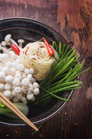 Oriental style lunch preparattion: mi trung egg noodles, chili pepper, moyashi, bok choi, moyashi springs and shimeji mushrooms in black vintage japanese bowl on the rustic wooden boardの写真素材