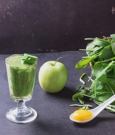 Glass of refreshing green smothie served with green apple, baby spinach leaves, soya sprouts and an egg yolkの写真素材