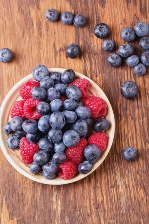 Blueberries and raspberries on a creamy vintage ceramic plate on natural rustic wooden boardの写真素材