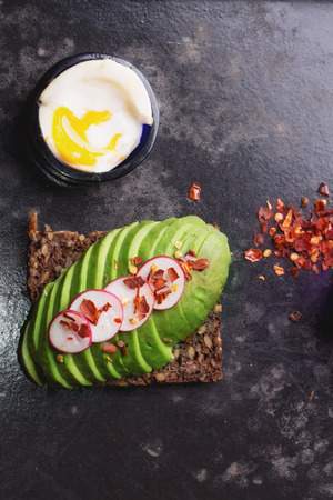 Open sandwich: avocado with raddish and chili flakes, soft boiled egg and chili flakes in a bowlの写真素材