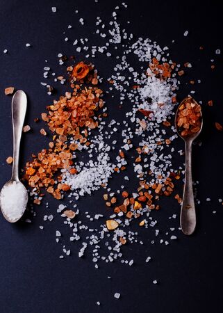 Sifting sea salt  and Himalayan rose rock salt with chili spices in vintage spoons over black background.の写真素材