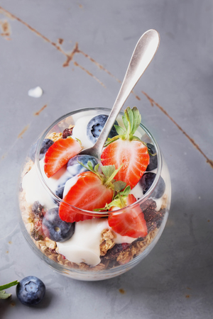Home made granola breakfast with strawberries and bluberries and plain yogurt, served in the glasses over a blue metal backgroundの写真素材