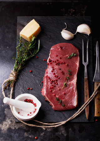 Raw fresh meat Striploin steak and seasoning on blackslate board over dark metal background, top viewの写真素材