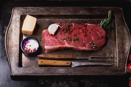 Raw fresh meat Striploin steak and seasoning on a rustic metal tray over dark metal background, top viewの写真素材