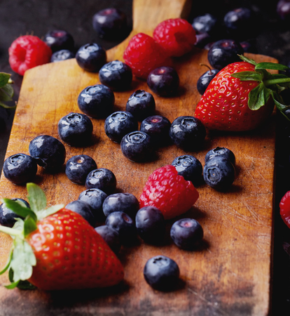 Organic blueberries served in the vintage cutting board over a black slate board and dark metal background. Dark Rustic Style.の写真素材