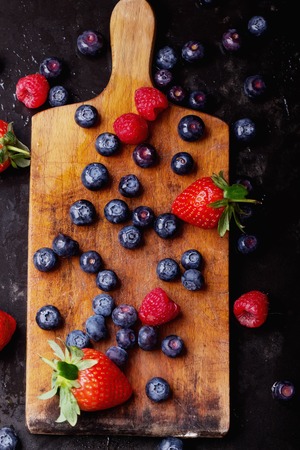 Organic blueberries served in the vintage cutting board over a black slate board and dark metal background. Dark Rustic Style.の写真素材