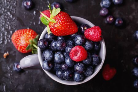 Organic blueberries served in the grey vintage cup over a black slate board and dark metal background. Dark Rustic Style.の写真素材