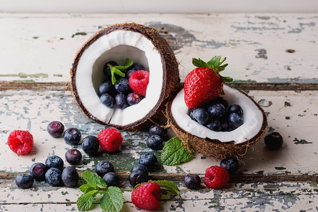 Organic berries: blueberries and strawberries served in two coconuts on a light wooden rustic, background. Concept of healthy food. Top view. Selective Focusの写真素材