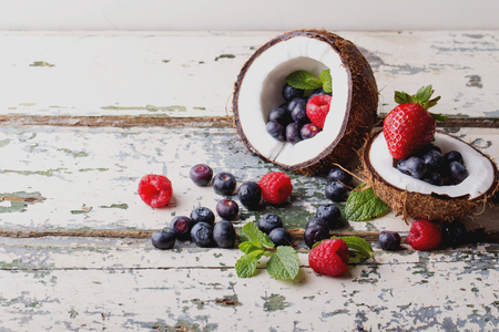Organic berries: blueberries and strawberries served in two coconuts on a light wooden rustic, background. Concept of healthy food. Top view. Selective Focusの写真素材