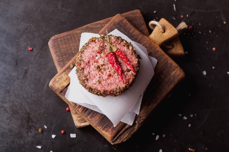 Raw Ground beef meat Burger steak cutlets  with chili and seasoning on  rustic wooden board over...