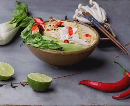 Japanese  bowl of ramen soup with tofu cheese, noodles, bok choi, smimeji  seaweed, chili, and lime  served with turquoise chopsticks over metal table. Dark rustic style. Top viewの写真素材