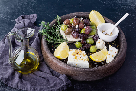 Traditional Greek and Middle east appetizer, various olives  and Feta cheese served with fresh pita bread, herbs,  seasoning and lemon in vintage cermic plate over a rustic black board background.の写真素材