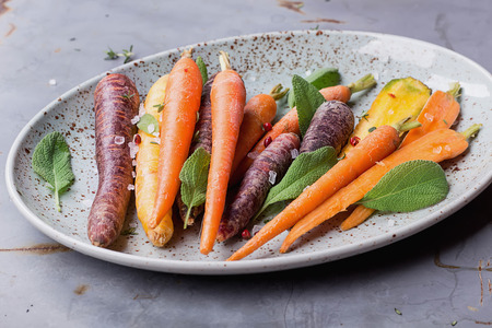Ready for baking peeled colorful raw carrots with fresh thyme herb,  with salt pepper and balsamic vinegar cream on the spotted vintage ceramic plate over metal surface. Top view.の写真素材
