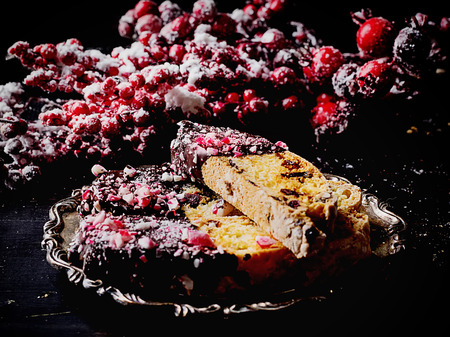 Home made biscotti decorated with dark chocolate and crushed candy cane on rustic metal serving plate with red decoration. Black background. Dark Rustic Styleの写真素材