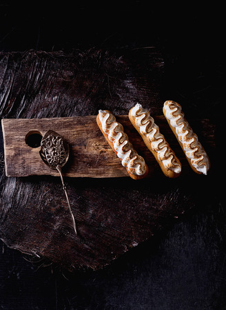 Home made eclairs decorated with white meringue on the rustic wooden serving board with cake...