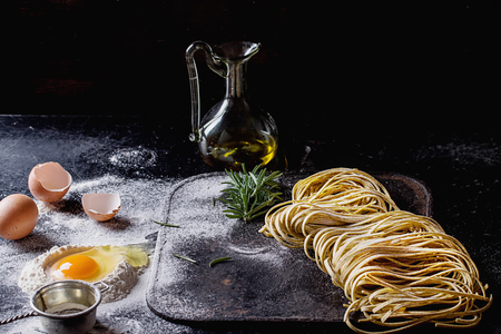 Raw uncooked black pepper spaghetti pasta with flour, egg rosemary, salt and spices and olive oil on vintage metal board over dark background. Space for text.の写真素材