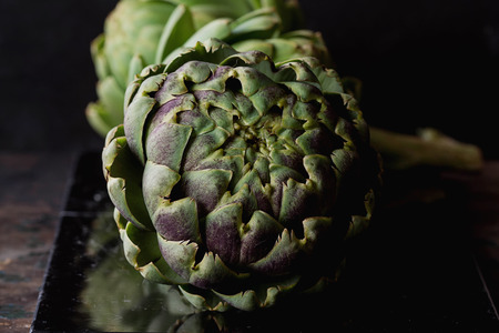 Fresh organic artichokes on a marble board  over a rustic wooden background. の写真素材