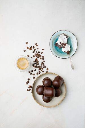 Whole and cracked Chocolate covered marshmallows, german "Schokokuss" or "Schokoschaumkuss" and glass of fragrant coffee over marble background with scattered roasted coffee beans. Top view.の写真素材