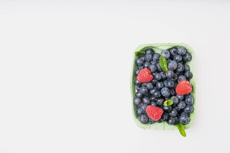 Ripe and juicy fresh blueberries decorated with mint leaves and raspberries in the box over white backgrounds. Top viewの写真素材