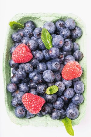 Ripe and juicy fresh blueberries decorated with mint leaves and raspberries in the box over white backgrounds. Top viewの写真素材