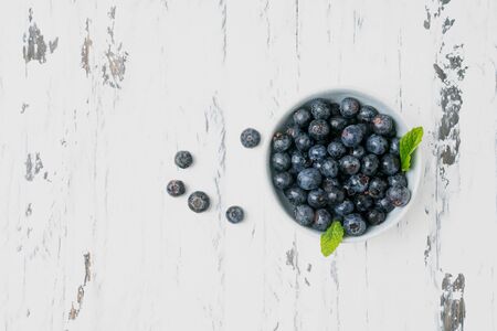 Ripe and juicy fresh blueberries decorated with mint leaves in the bowl over white rustic wooden backgrounds. Top viewの写真素材