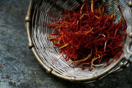 Dried saffron spice threads in vintage strainer over rustic metal background. Selective focus. Close up view.の写真素材
