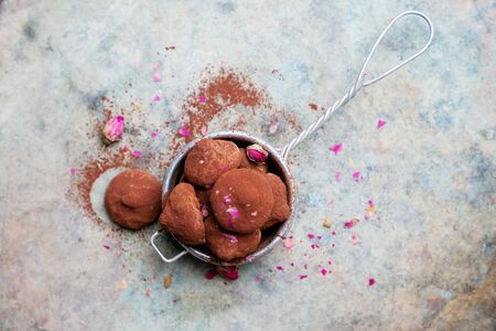 Chocolate candy truffles in tea strainer sprinkled with cocoa dust and flower petals over rustic metal background. Tasty confectionery collection. Top viewの写真素材