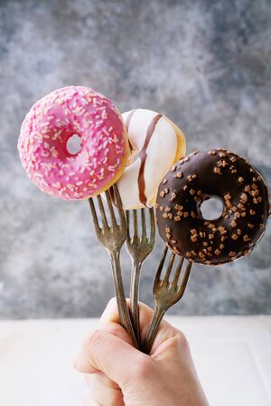 Glazed, chocolate frosted and sprinkled donuts on forks in her hand in front of rustic metal background. Close up view. Forks Madness setの写真素材