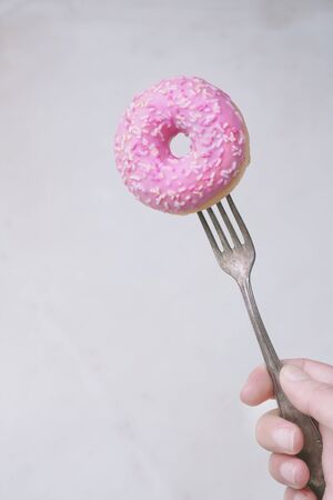 Pink frosted donut on a fork in her hand isolated on a marble background. Close up view. Forks Madness setの写真素材