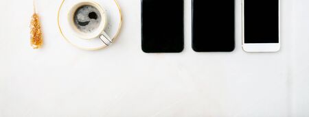 Three smartphones in a raw and cup of coffee over white background. Top view. Copy space.の写真素材
